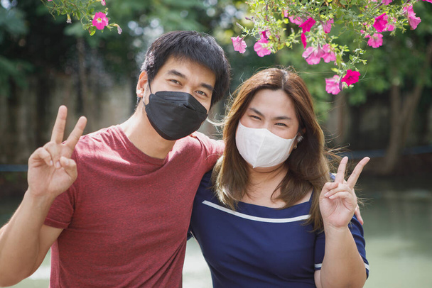 азіатська пара носить захисну маску для обличчя знак перемоги, що стоїть на відкритому повітрі
 - Фото, зображення