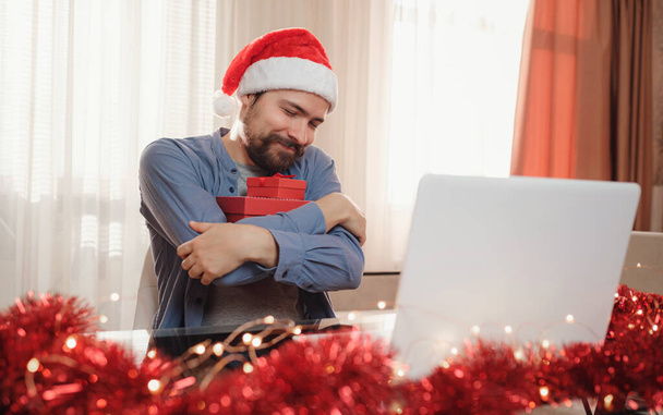 クリスマスに赤いカップのヒップスター男が家に座ってる。仮想クリスマス感謝祭ハウスパーティー。オンラインチームミーティング自宅からのビデオ会議コール. - 写真・画像
