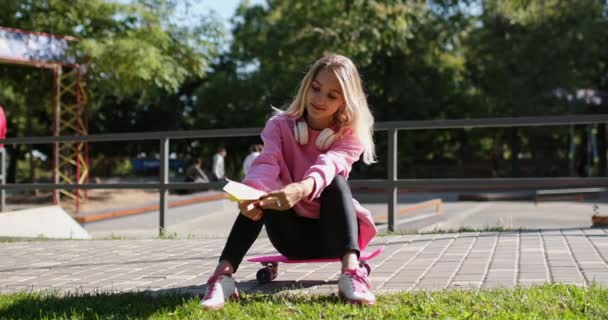 Woman launches paper plane sitting on penny board in park - Footage, Video