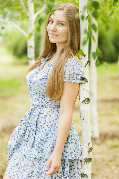 Portrait of a beautiful young woman with brown long hair on nature in a dress with a floral pattern. Girl resting in a birch forest - Fotoğraf, Görsel