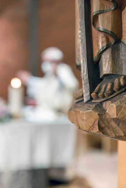 Резные деревянные ноги, детали деревянной статуи святого. На расплывчатом фоне священник служит мессу. - Фото, изображение