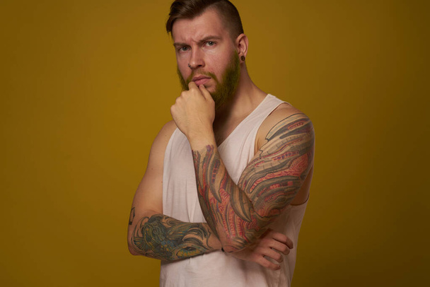 hombre barbudo en camiseta blanca con tatuajes en sus brazos posando mirada seria - Foto, imagen