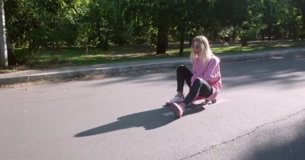 Młoda kobieta siedzi na tablicy penny jazdy na stoku Park Road - Materiał filmowy, wideo