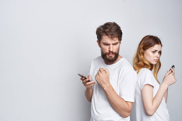 Beyaz tişörtlü evli bir çift ellerinde telefonlar stüdyo yaşam tarzıyla - Fotoğraf, Görsel