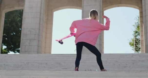 Frau tanzt mit Penny-Brett in der Hand auf Treppe nahe Bogen - Filmmaterial, Video