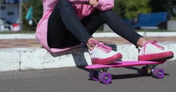 Woman plays with penny board sitting on curb by sidewalk - Footage, Video