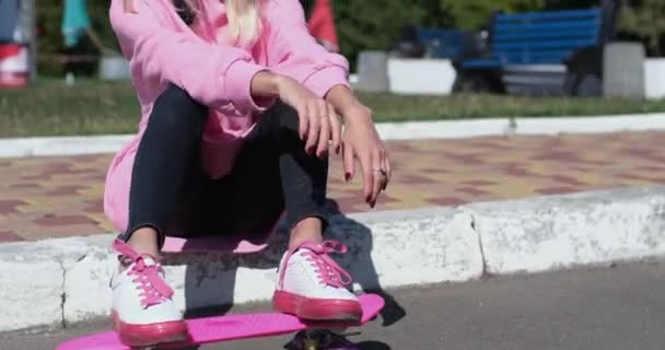 Young woman in helmet plays with penny board sitting on curb - Footage, Video