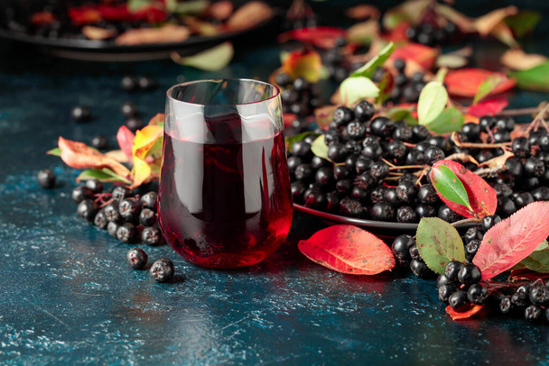 Black chokeberry juice and fresh berries on a dark blue background. - Fotoğraf, Görsel