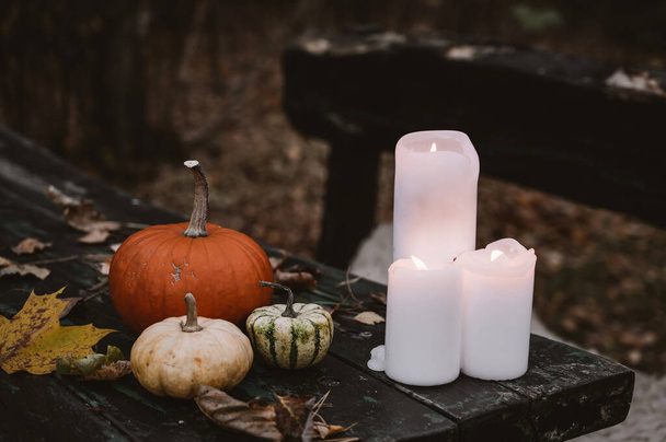 White burning candles, pumpkins and fallen leaves on old wooden table. Autumn halloweeen concept. - Фото, изображение