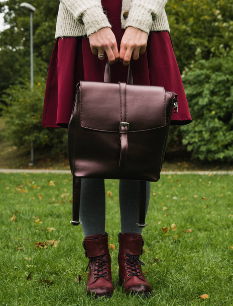Front view of female legs in grey tights and skirt. Stylish burgundy shoes. Leather bag in the arms. Green grass. Autumn fashion. - Foto, Bild