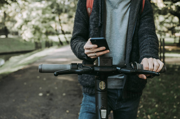 Uomo in possesso di un telefono e utilizzando l'app mobile per noleggiare scooter elettronico. Primo piano. Trasporto urbano ecologico moderno. - Foto, immagini