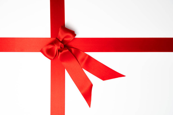 Kerstcadeau, Valentijnsdag of Black Friday concept: Rood cadeau lint gebonden in een strik op een witte achtergrond. Tafelaanzicht, vlakke lay, kopieerruimte. - Foto, afbeelding