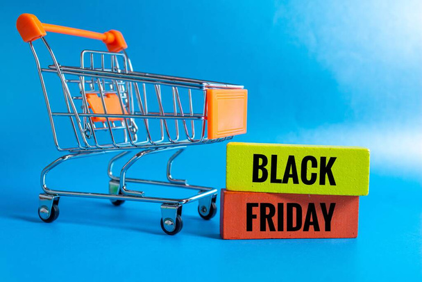Shopping cart and wooden blocks with black friday on it, Black friday concept idea photo. Isolated on bright blue background. - Fotografie, Obrázek