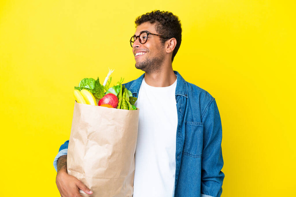 Junger brasilianischer Mann mit einer Einkaufstasche auf gelbem Hintergrund - Foto, Bild