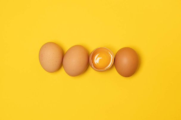 Organikus barna tyúktojás és egy törött tojás sárgával a háttérben. Minimális húsvéti koncepció. - Fotó, kép