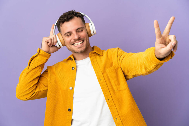 Jeune homme beau caucasien isolé sur fond violet écouter de la musique et chanter - Photo, image