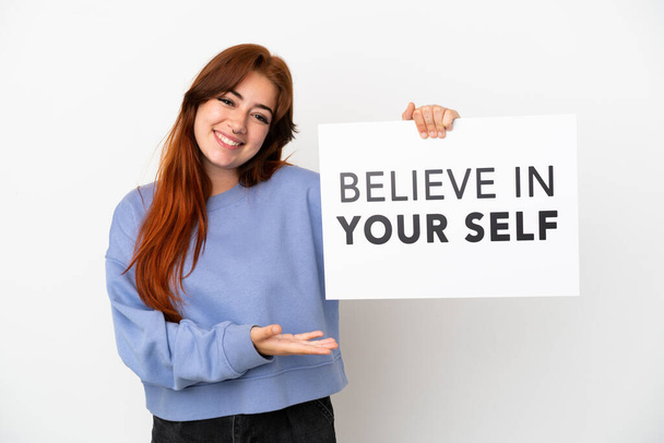 Fiatal vörös hajú nő elszigetelt fehér háttér kezében egy plakát szöveggel Higgy magadban és mutass rá - Fotó, kép
