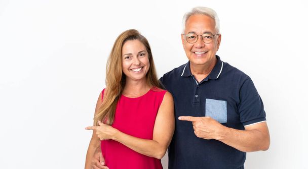 Paar mittleren Alters isoliert auf weißem Hintergrund zeigt mit dem Finger zur Seite und präsentiert ein Produkt - Foto, Bild
