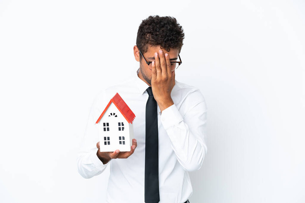 Young business Brazilian man holding a house toy isolated on white background with tired and sick expression - Фото, изображение