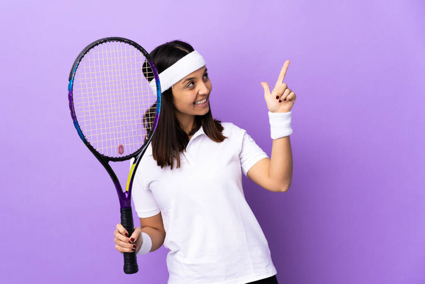 Junge Tennisspielerin über isolierten Hintergrund, die mit dem Zeigefinger auf eine großartige Idee zeigt - Foto, Bild