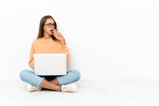 Молода жінка з ноутбуком сидить на підлозі позіхання і покриває широкий відкритий рот рукою
 - Фото, зображення