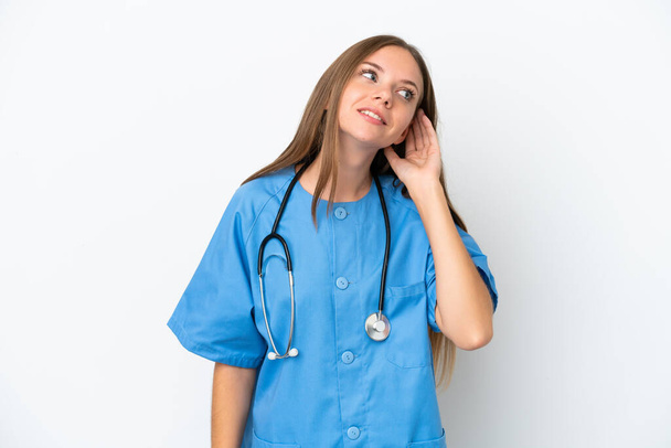 Joven médico cirujano mujer lituana aislada sobre fondo blanco escuchando algo poniendo la mano en la oreja - Foto, imagen