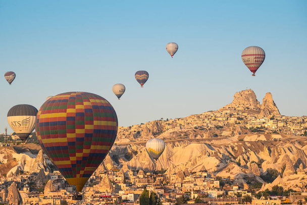 GOREME, TURQUIA - AGOSTO 5, 2021: Balões coloridos de ar quente sobrevoando a cidade de Goreme, na Capadócia, na luz da manhã, com o Castelo de Uchisar no fundo distante - Foto, Imagem