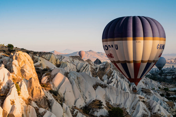 GOREME, TURKEY - AUGUST 3, 2021: Színes hőlégballonok repülnek nagyon közel a földhöz a Cappadocia-völgy felett a reggeli fényben - Fotó, kép