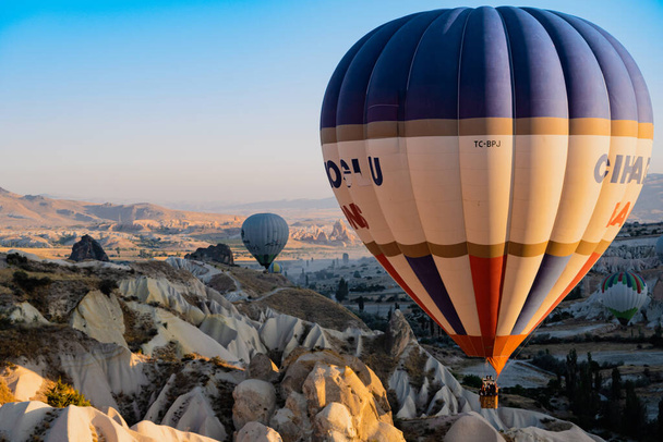 GOREME, TURCHIA - 3 AGOSTO 2021: Palloncini colorati che volano molto vicino al suolo sulla valle della Cappadocia alla luce del mattino - Foto, immagini