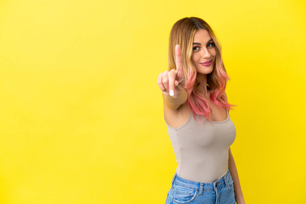 Young woman over isolated yellow background showing and lifting a finger - Фото, изображение