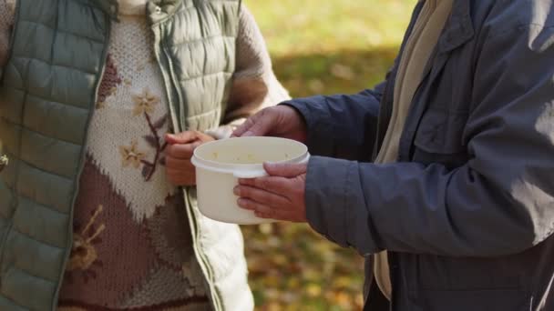 Sociální péče. Charitativní akce. Žena nalévání horké polévky v plastovém obalu v rukou oldman - Záběry, video