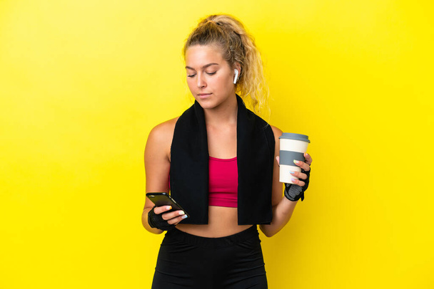 Sportlerin mit Handtuch isoliert auf gelbem Hintergrund mit Kaffee zum Mitnehmen und einem Handy - Foto, Bild