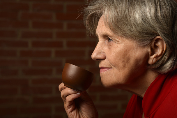 Elderly woman red drinking coffee - Фото, изображение