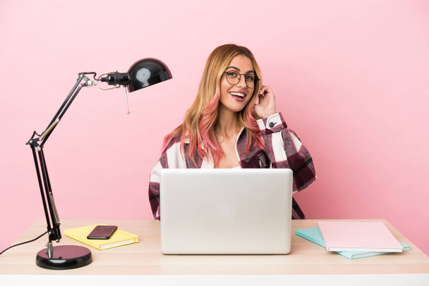 Jovem estudante mulher em um local de trabalho com um laptop sobre fundo rosa rindo - Foto, Imagem