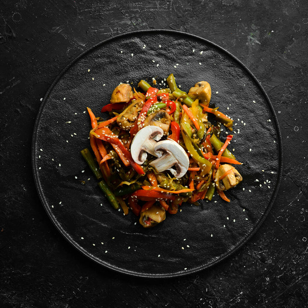 Baked wok vegetables on a black stone plate. Asian cuisine. Top view. - Fotó, kép