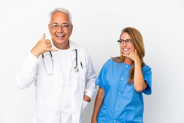 Médico y enfermera de mediana edad aislados sobre fondo blanco haciendo gesto telefónico. Llámame señal de vuelta - Foto, Imagen