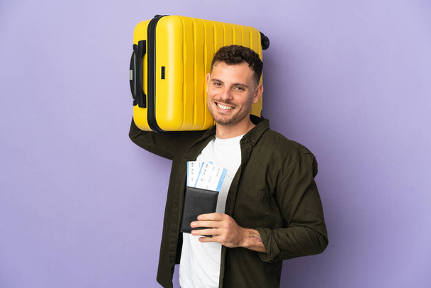 Jovem caucasiano bonito homem isolado no fundo branco em férias com mala e passaporte - Foto, Imagem