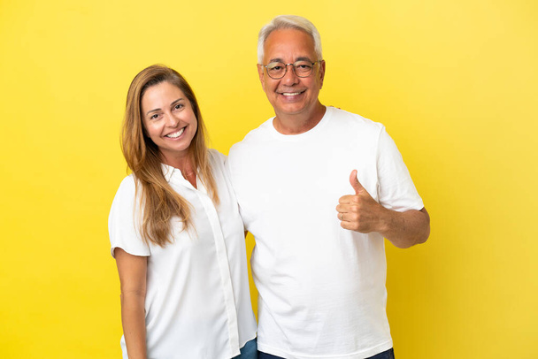 Middelbare leeftijd paar geïsoleerd op gele achtergrond geven een duim omhoog gebaar - Foto, afbeelding