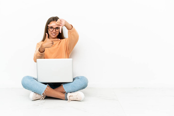 Egy fiatal nő laptoppal a padlón, fókuszáló arccal. Keretezési szimbólum - Fotó, kép