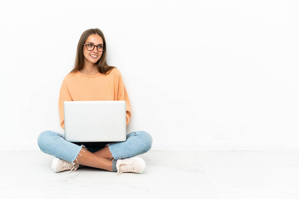 Jonge vrouw met een laptop zittend op de vloer met gekruiste armen en gelukkig - Foto, afbeelding