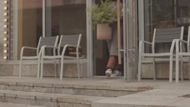 Gesperrter niedriger Winkel von Restaurantmitarbeitern, die Blumentöpfe nehmen und sie morgens vor der Öffnung im Freien aufstellen - Filmmaterial, Video