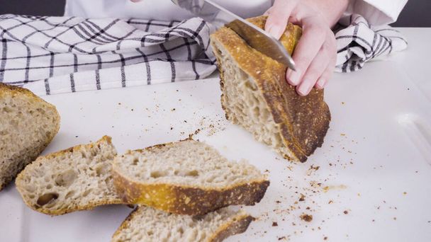 Beyaz bir kesme tahtasının üzerinde taze ekşi ekmek dilimliyorum.. - Fotoğraf, Görsel