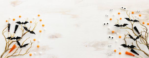 ハロウィーンの最高の景色の画像。白い木製のテーブルの上に魔女のほうきや裸の木やお菓子やコウモリ - 写真・画像