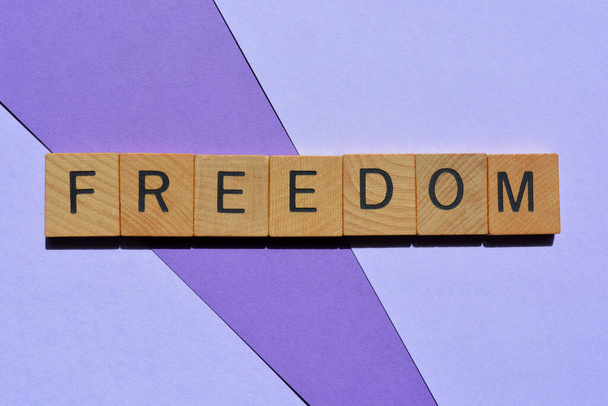 Wolność, słowo w drewnianych liter alfabetu izolowane na fioletowym tle - Zdjęcie, obraz