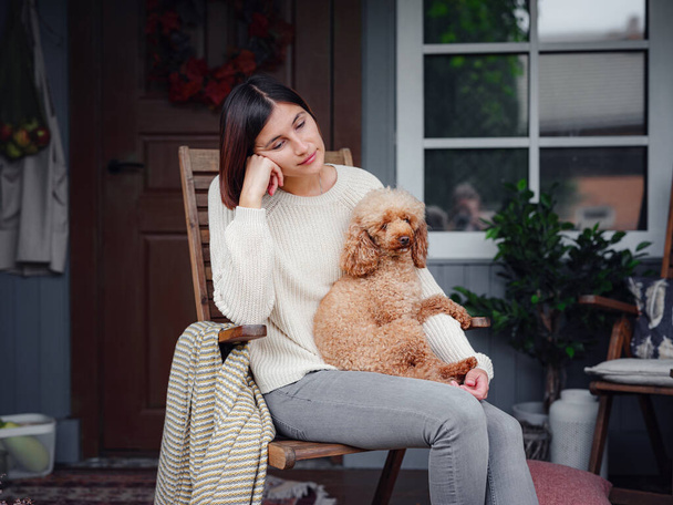 Mujer asiática joven descansando al aire libre con una taza de café en el porche de la casa de campo, relajándose afuera con perro caniche. estilo de vida de otoño, ocio concepto de tiempo libre. Copiar espacio - Foto, imagen