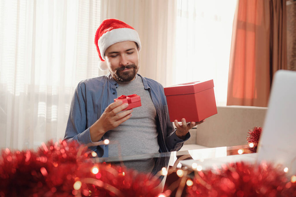 Hipster muž s červeným pohárem sedí doma o Vánocích. Virtuální vánoční oslava díkůvzdání. Online tým setkání videokonference volání z domova. - Fotografie, Obrázek