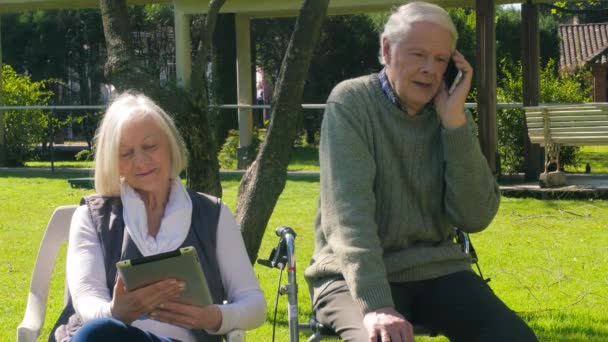 Feliz pareja de ancianos relajándose al aire libre haciendo llamadas telefónicas. Personas mayores activas - Imágenes, Vídeo