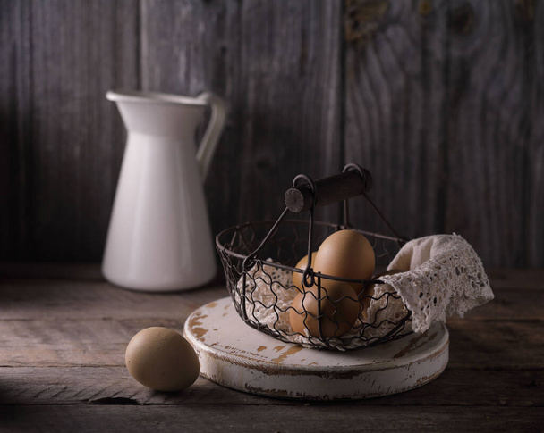 Still life with fresh chicken eggs in a wicker basket on a wooden table. - Foto, afbeelding