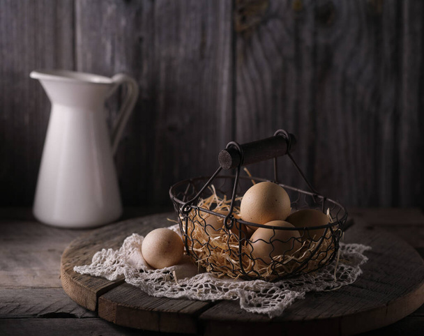 Still life with fresh chicken eggs in a wicker basket on a wooden table. - Foto, afbeelding