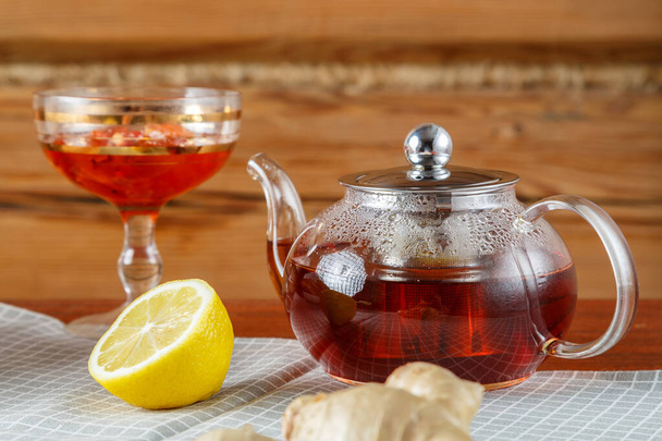 A glass teapot with tea is on the table against the background of a wooden wall. Horizontal photo - Φωτογραφία, εικόνα